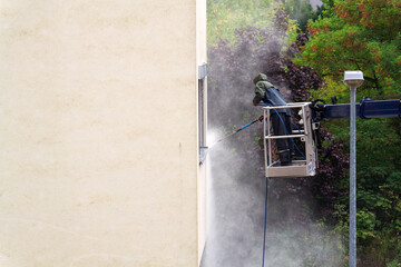 Unrecognizable man cleaning facade surface from lifting platform with high pressure stream of water