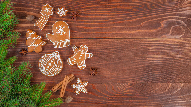 Christmas gingerbread cookies with icing, fir branches and cinnamon sticks on wooden table, festive holiday background with traditional handmade sweets and copy space for text - Powered by Adobe