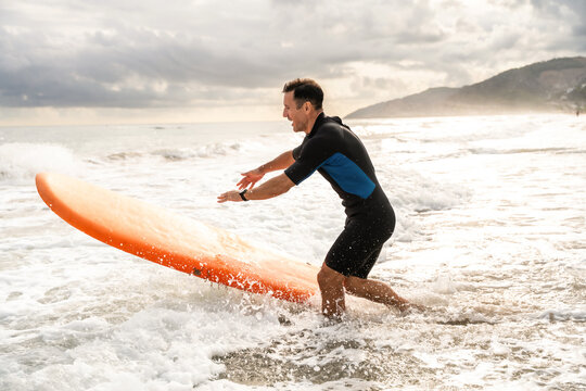 Mature sportive man learning surfing running on beach with surfboard