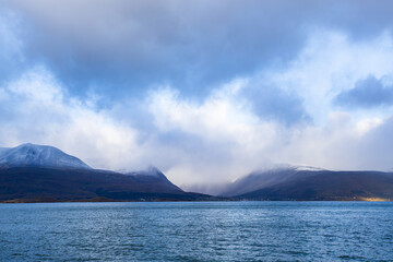 Autumn landscape of the Lyngen Alps in Northern Norway with snowy peaks, dramatic clouds, and a tranquil fjord.