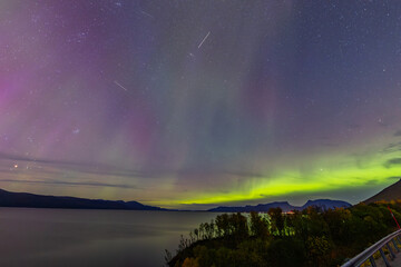 Northern lights in Kiruna, Sweden, reflecting on calm water in September with stars and forest in the background.