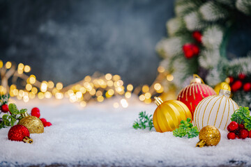 Naklejka na ściany i meble Christmas Holiday background with snow, fir tree and decorations with christmas light behind. Christmas red, white and golden balls on a winter festive background.