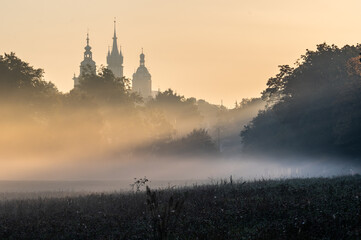 Foggy sunrise on Blonia meadow in Krakow, Poland, with St Mary's church and Town Hall towers in the background,