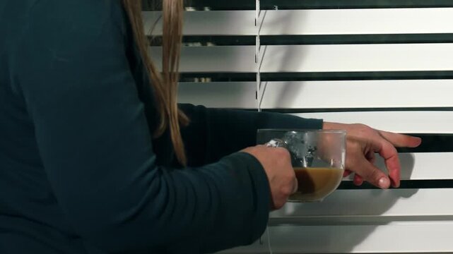 Woman opening window blinds nervously