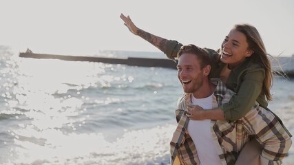 Young fun couple two friends family man woman wear shirt casual clothes together giving piggyback ride to joyful, sit on back rest relax in free time walk on sea sand shore beach seaside in summer day