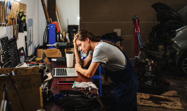 Tired and depressed female professional at auto repair garage. Small business and financial crisis.