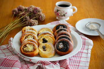 Traditional Czech festive kolache with apple, curd cheese and poppy seed filling sprinkled with powdered sugar served on plate with coffee cup and dried allium bouquet, sweet homemade bakery pastry