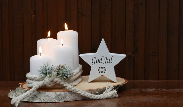 Christmas greeting card: White candles decorated with Christmas baubles and a snowman on a wooden slice. The Swedish greeting "God jule" is written on a star.