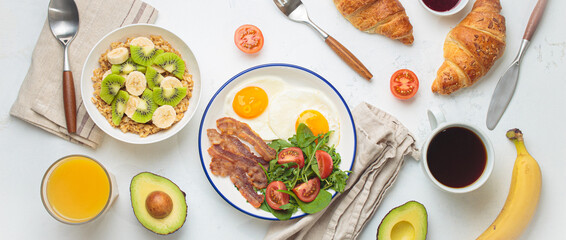 Breakfast table healthy foods fried eggs, bacon, oats fruit, avocado, croissants, coffee, orange...