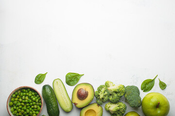 Fresh raw green vegetables and fruit white concrete background top view, diet, vegetarian food. Set of different green healthy products, clean eating nutrition space for text