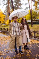 Charming couple enjoying a cozy moment outdoors in a city park during autumn. They share a joyful smile, conveying warmth and connection on a sunny day.