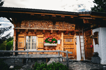 Fototapeta premium Rustic wooden mountain cabin with flower box and stacked firewood, traditional Swiss chalet architecture, cozy countryside home in the Alps, summer travel destination.