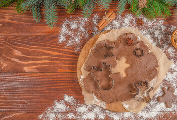 Christmas gingerbread dough with cookie cutters on parchment paper, wooden table sprinkled with flour, cinnamon sticks, fir branches holiday baking preparation, top view copy space