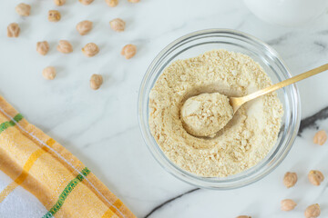 Gluten-free chickpea flour in a bowl with spoon on white marble kitchen table. Top view.