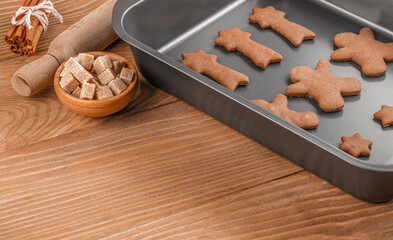 Raw gingerbread cookies on baking tray with brown sugar cubes, cinnamon sticks and rolling pin on...