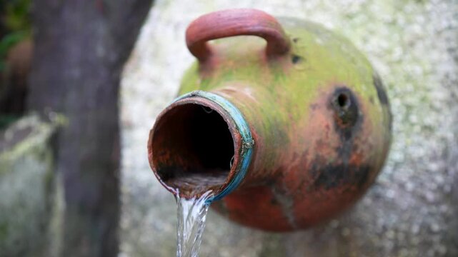 Old clay jug fountain with flowing water on stone wall