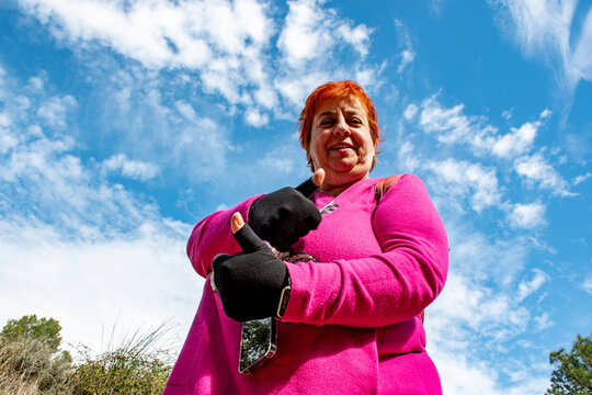 Mujer de 60 a&ntilde;os  alegre paseando por el bosque, foto contrapicado con nubes blancas y cielo azul