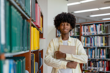 Young male student standing in library, confidently holding book and smiling in educational school.