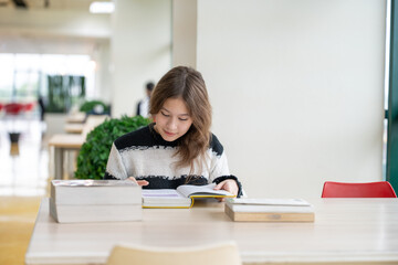Young woman reading book on table at library school