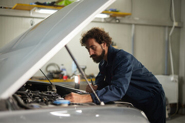 A car mechanic is focused on repairing a vehicle's engine in a clean garage. Tools and equipment are visible, creating an organized workspace.