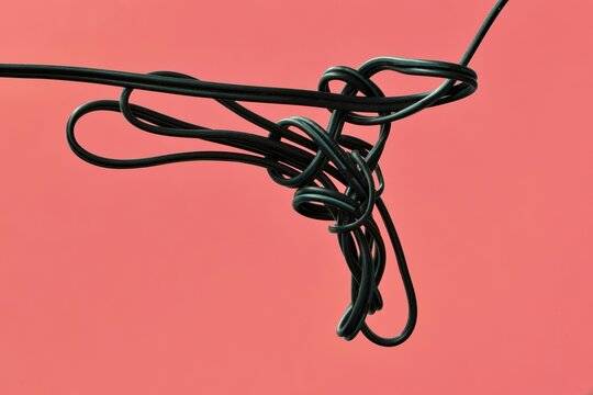Tangled cord electrical cable on plain pink background conceptual image.	