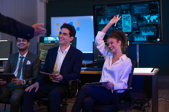 Group of professionals businesswoman and businessman in formal attire discussing ideas on innovative technology development project with tablets and laptops in dark modern office