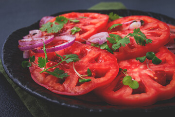 Freshly sliced tomatoes and red onions, garnished with herbs, on a black plate, summer salad, no people