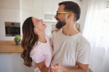 With laughter filling the air, a couple shares a happy moment in their modern kitchen. Morning light shines as they dance and connect.