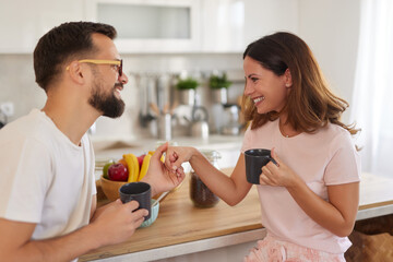 A couple shares a joyful moment in their kitchen, sipping coffee and engaging in a light-hearted conversation while surrounded by fresh fruit.