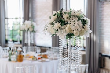 Close-up of a gorgeous wedding table centerpiece featuring a lush arrangement of white hydrangeas and roses, elevated on a clear vase with hanging crystal strands