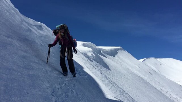 Solo woman mountaineer hiking snowy ridge with backpack and ice axe, alpine adventure and outdoor exploration concept