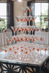 Close-up of a classic champagne tower or cocktail pyramid with martini glasses filled with an orange beverage and cherries, ready for a wedding reception