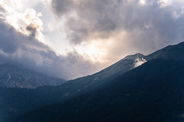 Dramatic cloudy sunrise over misty alpine mountain ridge