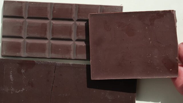 Hand placing a bar of craft chocolate. Unwrapped chocolate bars background. Broken chocolate. Different shades of brown. Top view.