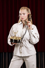 A beautiful blonde in a beige suit holds an old desk telephone. Close-up against a theater curtain.