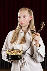 A young, beautiful woman holds an old desk telephone. Close-up against a theater curtain.