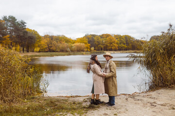 Charming couple enjoying a cozy moment outdoors in a city park during autumn. They share a joyful smile, conveying warmth and connection on a sunny day.