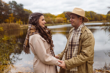 Charming couple enjoying a cozy moment outdoors in a city park during autumn. They share a joyful smile, conveying warmth and connection on a sunny day.