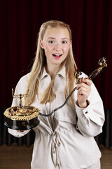 A young, beautiful woman holds an old desk telephone. Close-up against a theater curtain.
