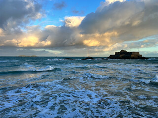 Golden sunlight illuminates waves and fortress under dramatic clouds, perfect for travel, tourism, and design use