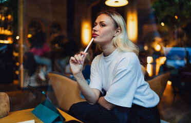 Creative freelancer pauses with pen to lips, reflecting on ideas while working digitally. Emphasizes concept development and thoughtful engagement with mobile technology