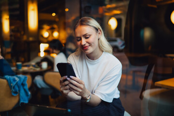 Smiling woman looks at smartphone with warm focus, fully engaged in digital activity. Captures connection, calm joy, and seamless integration of personal tech in daily routine
