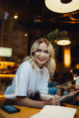 Stylish young woman smiles as she draws on tablet using stylus, enjoying a moment of creative digital flow while immersed in tech-focused remote work setting