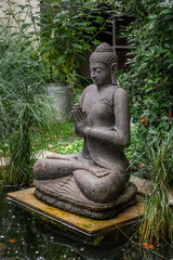 Image of an nn aged statue of Buddha popularly employed as garden ornament. A garden design or landscaping concept.