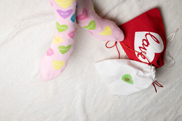 Valentine's Day celebration.  Woman wearing pink socks with pastel conversation hearts on a white faux fur bed covering with gifts.