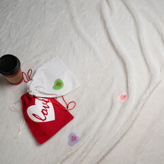 Valentine's Day gifts and a coffee on a white, faux fur blanket on bed, view from above with copy space.