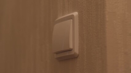 From darkness to light, a close-up of a man's hand turning on the light in a room while inside pressing an electrical switch on the wall