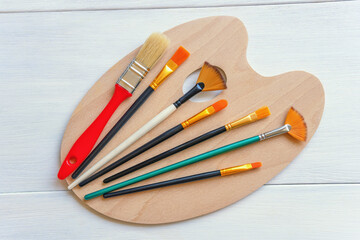 Art palette and various types of artistic paintbrushes on rustic table