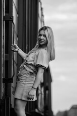 Young woman with long hair stands confidently beside a train on railway tracks, wearing casual attire, showcasing a blend of urban lifestyle and transportation themes