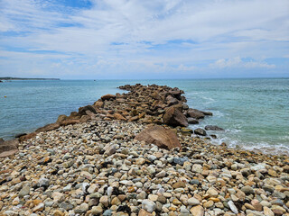 Scenic natural rock jetty extending into the turquoise ocean at Punta de Mita beach, Nayarit, Mexico, framed by a pebbly shore under a clear sky.